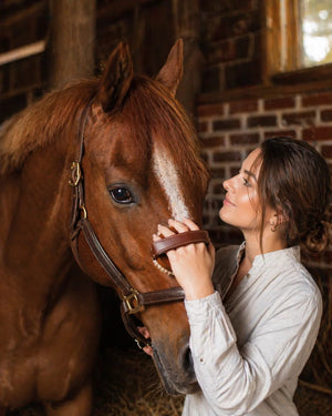 Woman petting a brown horse in a stable with brick walls.
