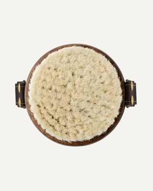 Round beige scrubber with wooden handle on a white background